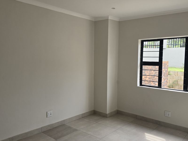A clean, empty bedroom featuring neutral wall tones, tiled flooring, and large windows with security bars, offering a bright and versatile living space.