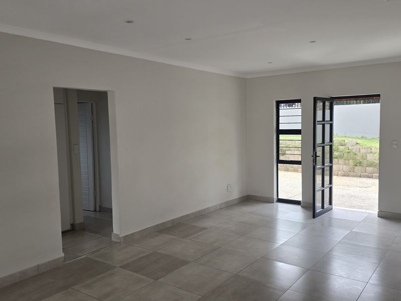 A bright, empty living room featuring large format floor tiles, recessed lighting, and direct access to the outdoor area through glass doors.