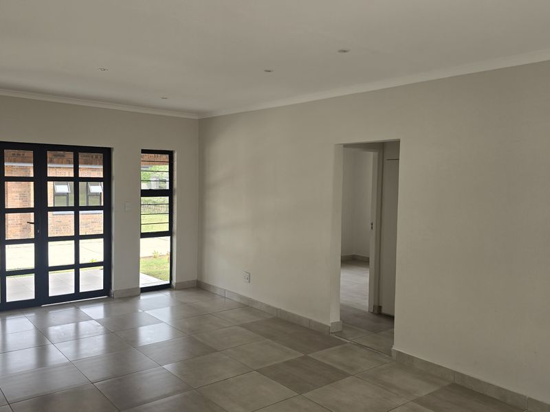 A bright and spacious open-plan living area featuring neutral tiled flooring, modern aluminium-framed glass doors, and recessed downlighting, offering a clean, blank canvas.