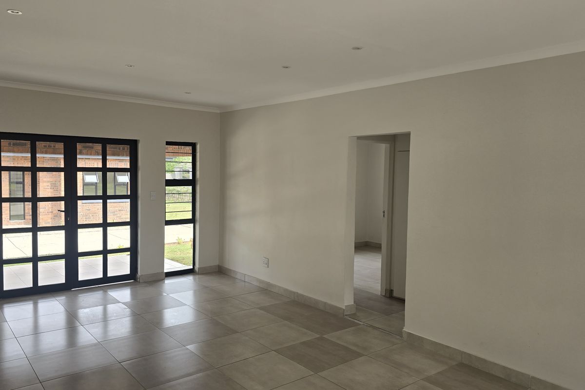 A bright and spacious open-plan living area featuring neutral tiled flooring, modern aluminium-framed glass doors, and recessed downlighting, offering a clean, blank canvas.