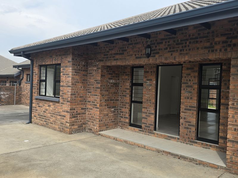 A well-maintained face brick townhouse exterior featuring a tiled roof, aluminium window frames, and a paved entrance area.