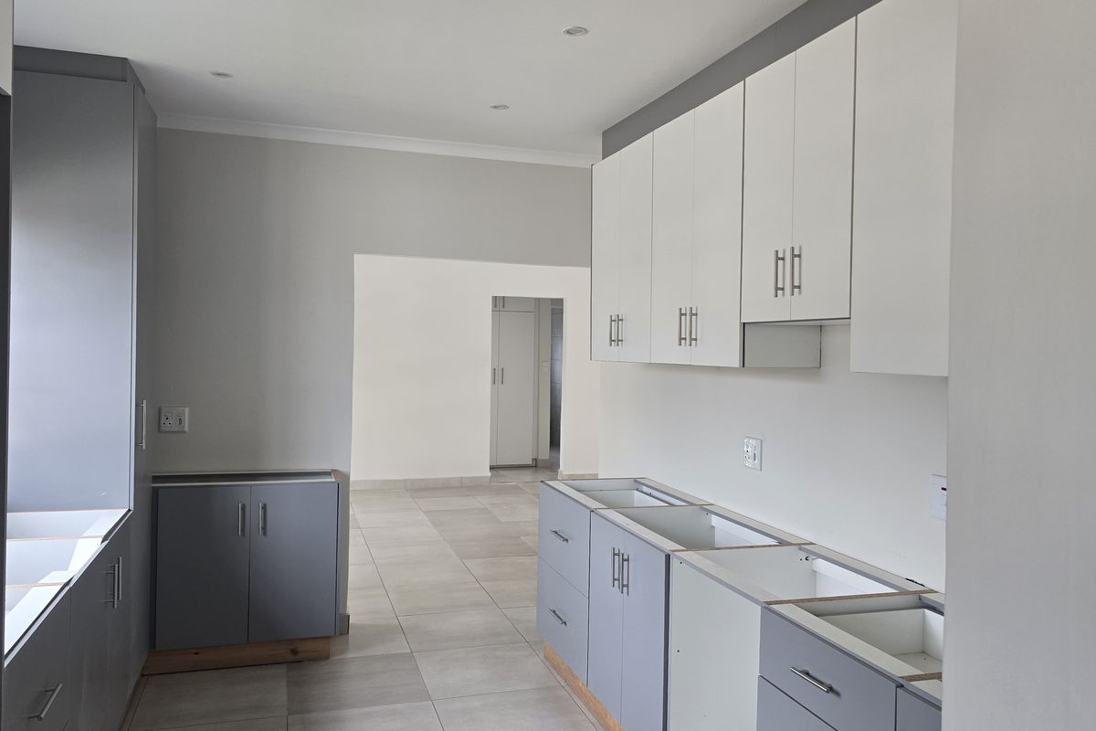 A modern, unfinished kitchen space featuring grey and white cabinetry, tiled flooring, and recessed lighting, awaiting countertops and appliances to complete the installation.