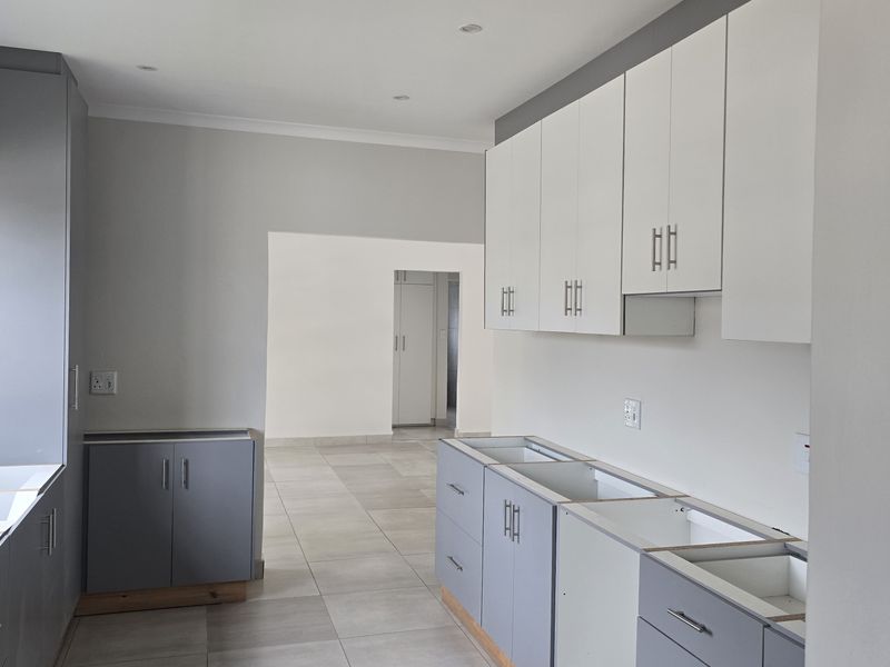 A modern, unfinished kitchen space featuring grey and white cabinetry, tiled flooring, and recessed lighting, awaiting countertops and appliances to complete the installation.
