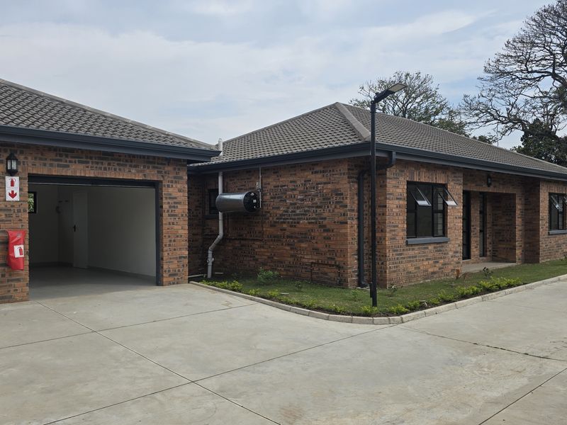A well-maintained face brick townhouse featuring a concrete tile roof, integrated garage, and paved driveway in a clean, modern estate setting.