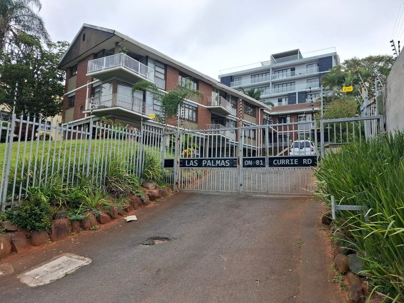 Front entrance view of Las Palmas apartment complex featuring a secure gated driveway, brick building facade, and multiple balconies.