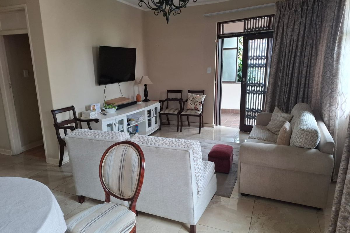 A comfortable living room featuring tiled flooring, a decorative chandelier, and direct access to an outdoor patio area through a secure sliding door.