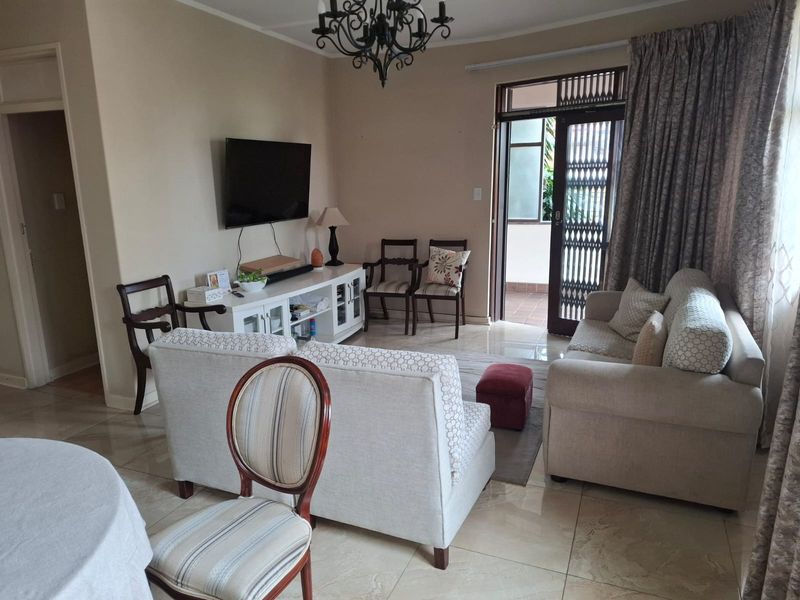 A comfortable living room featuring tiled flooring, a decorative chandelier, and direct access to an outdoor patio area through a secure sliding door.