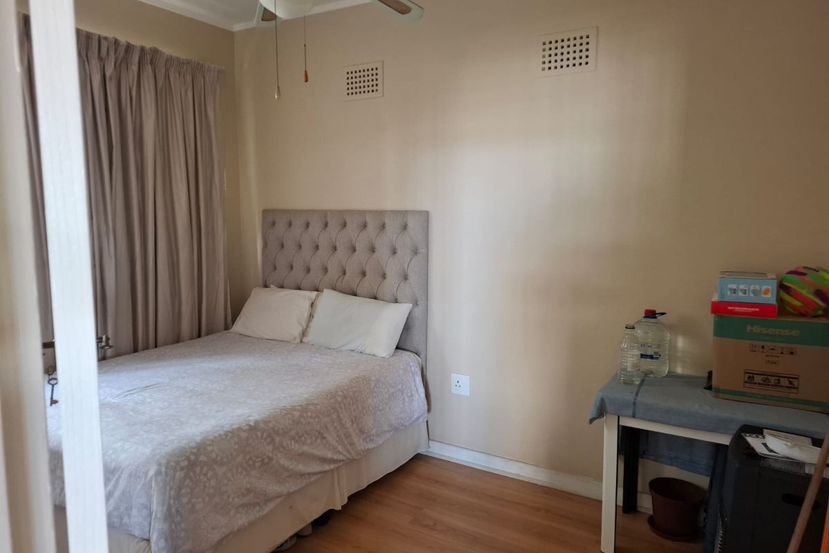 A functional bedroom featuring laminate flooring, a ceiling fan, and wall-mounted ventilation grilles, providing a neutral base for interior design updates.
