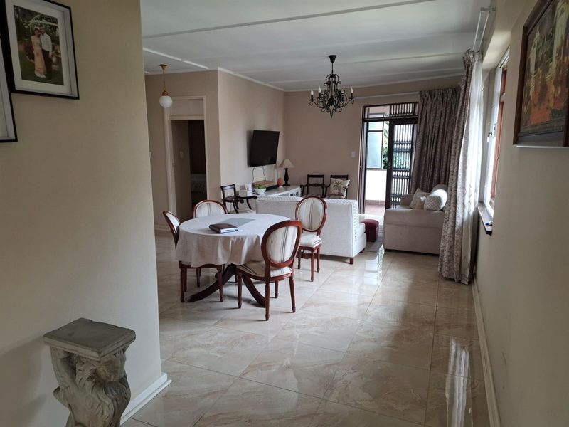 Open-plan living and dining area featuring polished tiled flooring, a central chandelier, and direct access to an outdoor balcony through a sliding glass door.