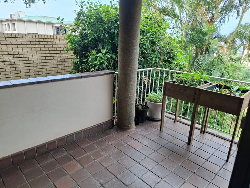 A covered balcony featuring tiled flooring, a brick boundary wall, and a metal balustrade, offering a functional outdoor space.
