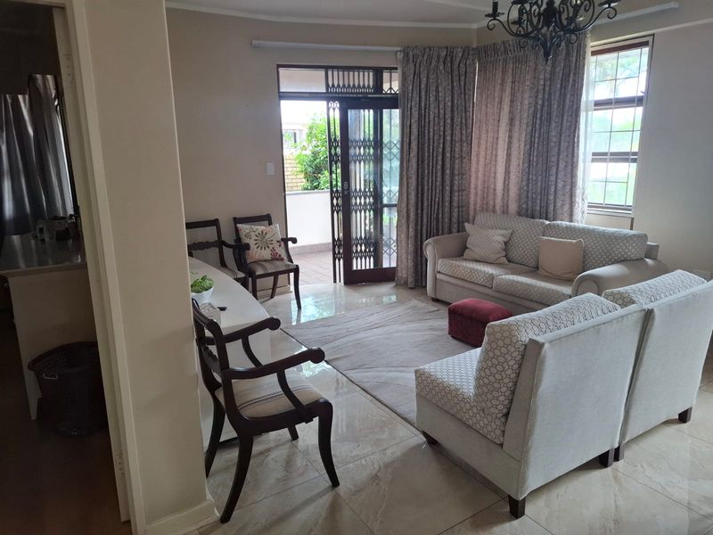 A bright living room featuring tiled flooring, a chandelier, and a security gate leading to an outdoor area.