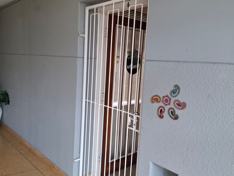A secure apartment entrance featuring a white metal security gate, a recessed wall niche, and a clean, painted exterior wall finish.