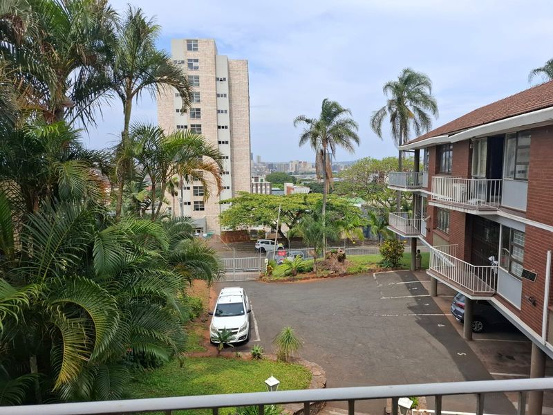 Elevated view overlooking the apartment complex grounds, parking area, and surrounding urban landscape.