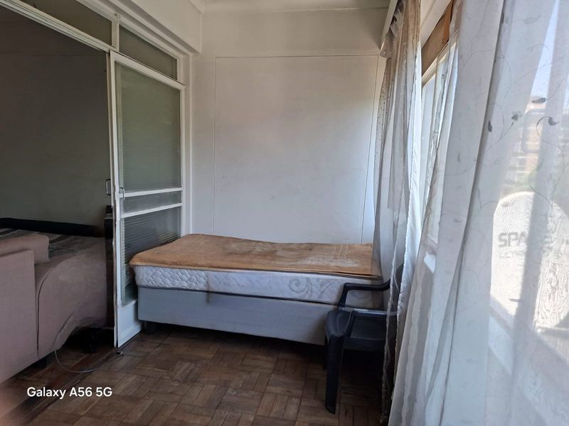 A compact bedroom featuring parquet flooring and a sliding glass door, currently in need of cosmetic updates and maintenance.