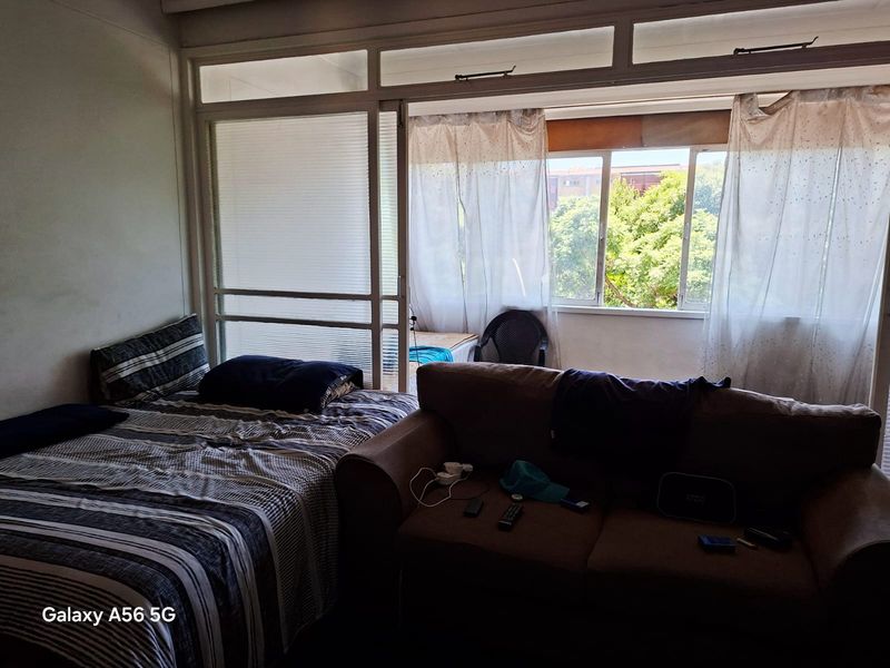 A bedroom featuring a large sliding glass door and window, providing natural light and access to an adjacent enclosed balcony area.