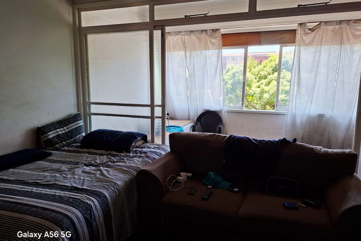 A bedroom featuring a large sliding glass door and window, providing natural light and access to an adjacent enclosed balcony area.