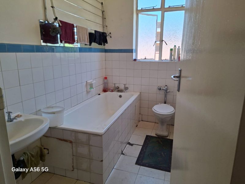 A dated bathroom featuring a bathtub, pedestal basin, and toilet with tiled finishes, requiring cosmetic updates and repairs to flooring and tiling.