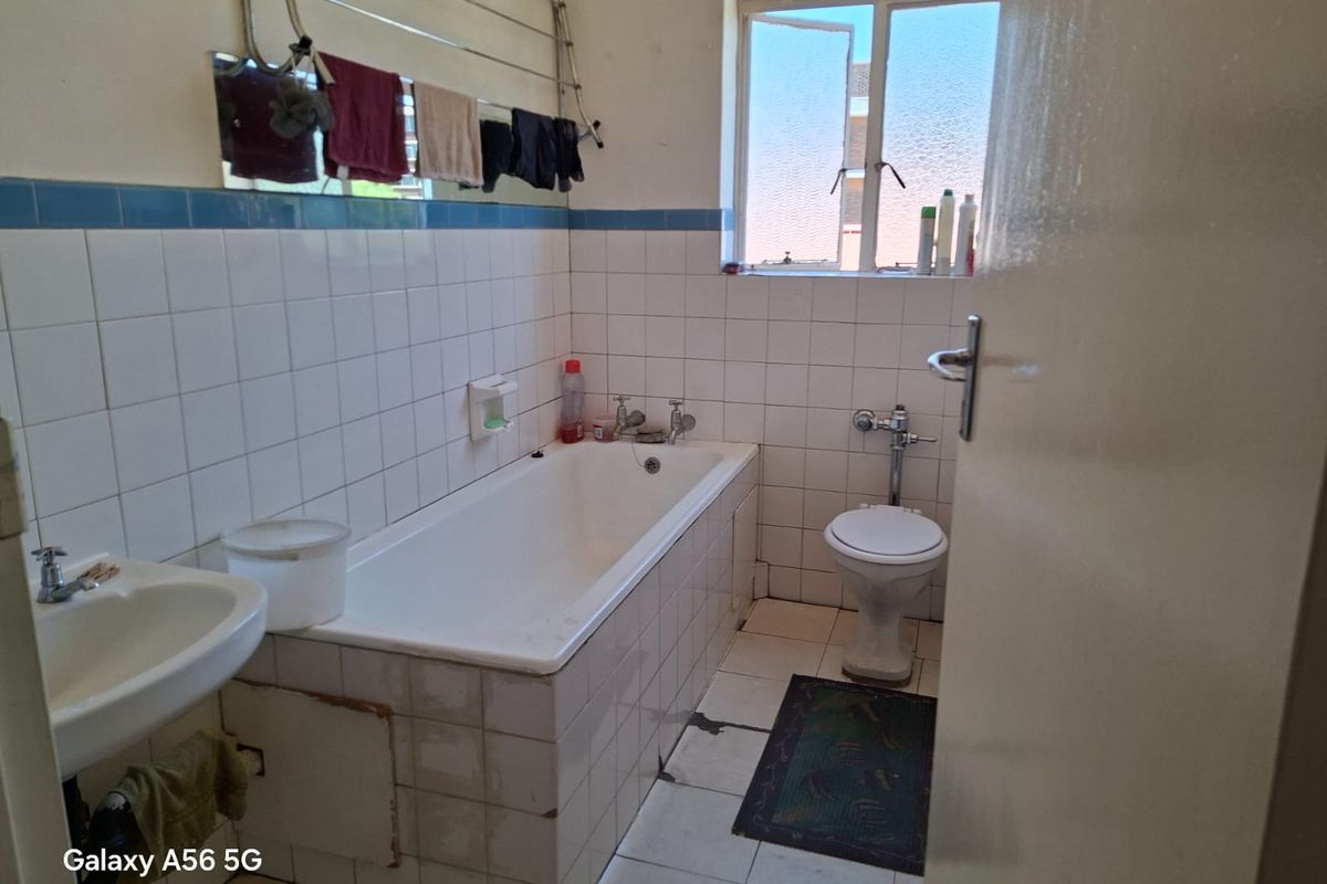 A dated bathroom featuring a bathtub, pedestal basin, and toilet with tiled finishes, requiring cosmetic updates and repairs to flooring and tiling.