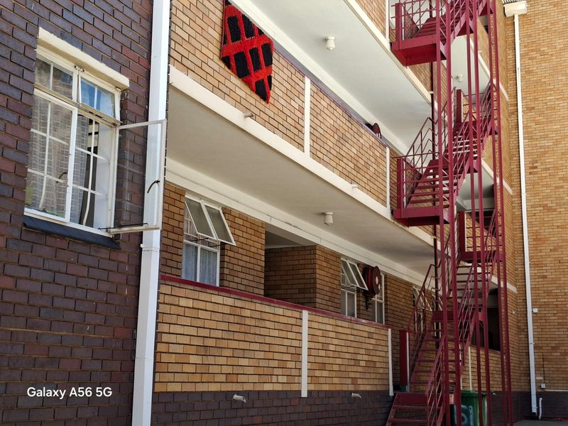 Exterior view of an apartment building featuring a brick facade and a prominent red external steel staircase providing access to upper levels.