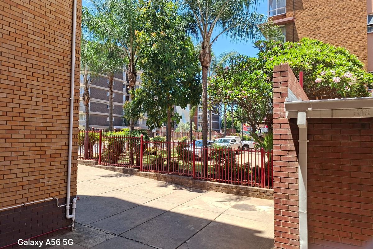A view of the apartment complex rear courtyard featuring brick walls, paved flooring, and established trees enclosed by metal fencing.