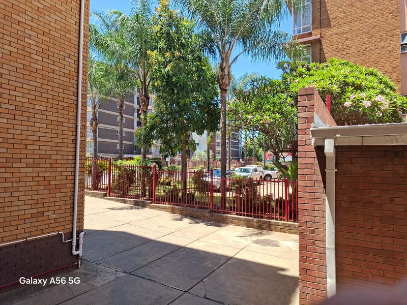 A view of the apartment complex rear courtyard featuring brick walls, paved flooring, and established trees enclosed by metal fencing.