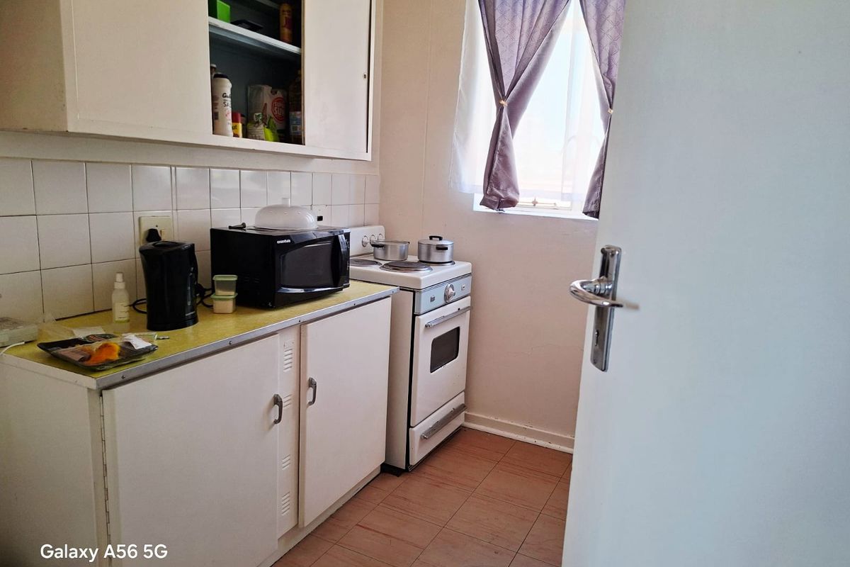A compact kitchen featuring dated cabinetry, a tiled backsplash, and a freestanding stove, offering potential for modernization and layout optimization.