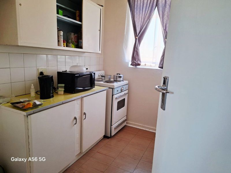 A compact kitchen featuring dated cabinetry, a tiled backsplash, and a freestanding stove, offering potential for modernization and layout optimization.