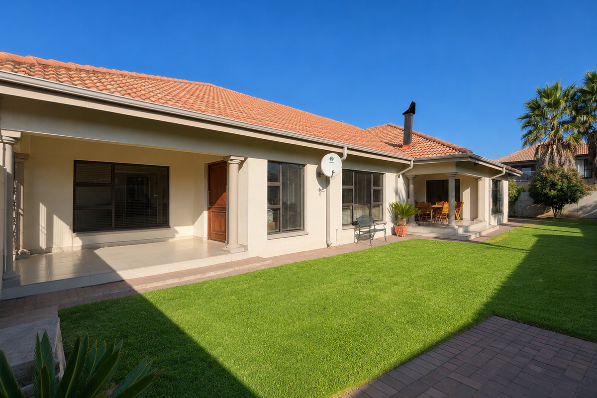 A well-maintained rear exterior view featuring a spacious covered patio, tiled roof, and a neatly landscaped lawn with paved pathways.