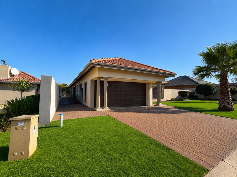 A well-maintained single-story residence featuring a paved driveway, double garage, decorative columns, and a neatly landscaped front garden.