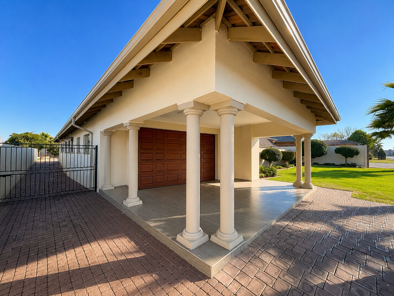 A well-maintained front exterior featuring a covered patio with classical columns, a paved driveway, and a secure wooden garage door.