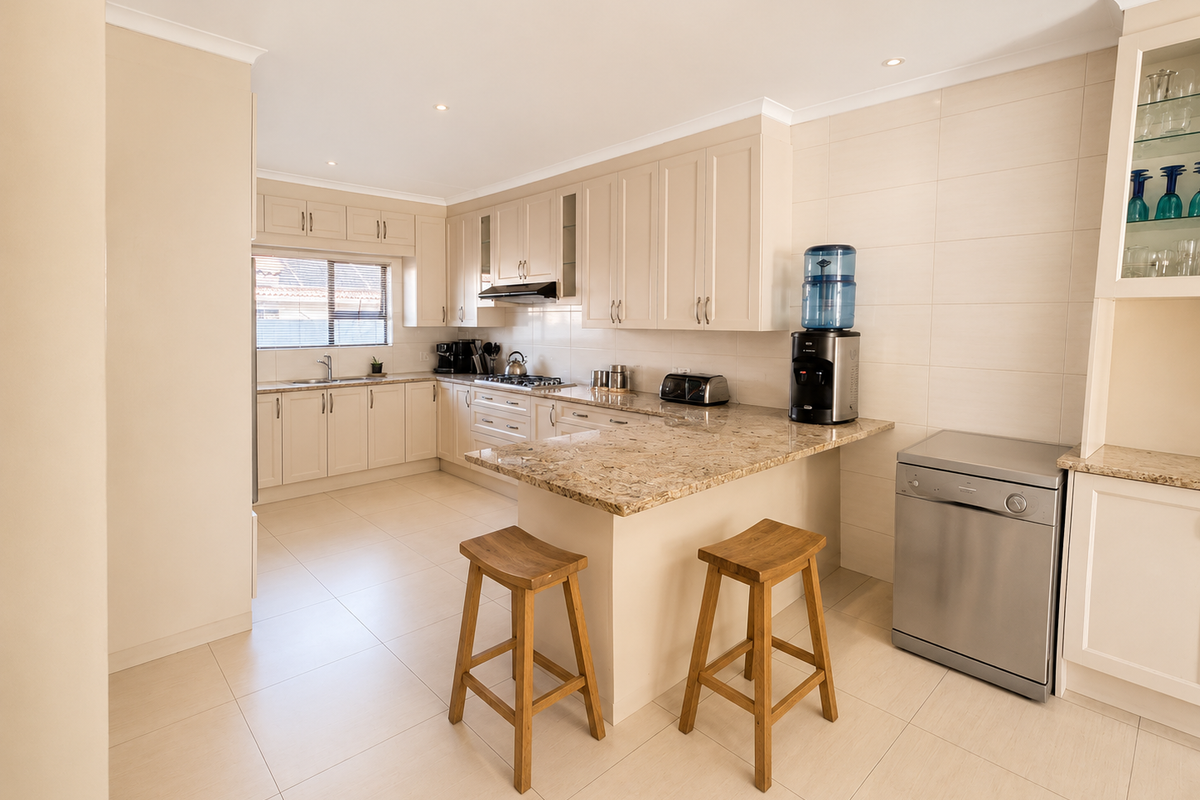 A well-maintained kitchen featuring granite countertops, ample built-in cabinetry, a gas hob with extractor, and a breakfast nook area with tiled flooring.