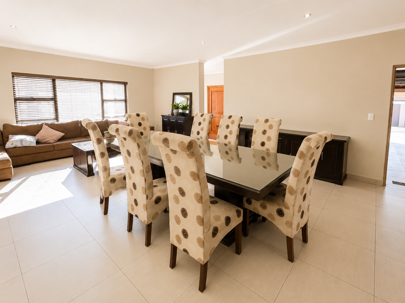 Spacious open-plan living and dining area featuring neutral tiled flooring, recessed lighting, and large windows with venetian blinds.