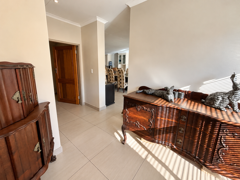 A bright hallway featuring neutral tiled flooring and a solid wooden door, leading through to an open-plan living area.