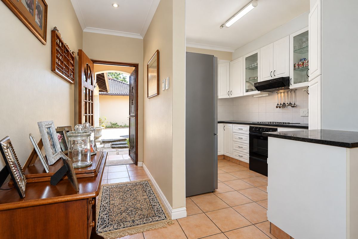 A functional kitchen featuring white cabinetry, dark stone countertops, tiled flooring, and integrated appliances, adjacent to the home entrance.