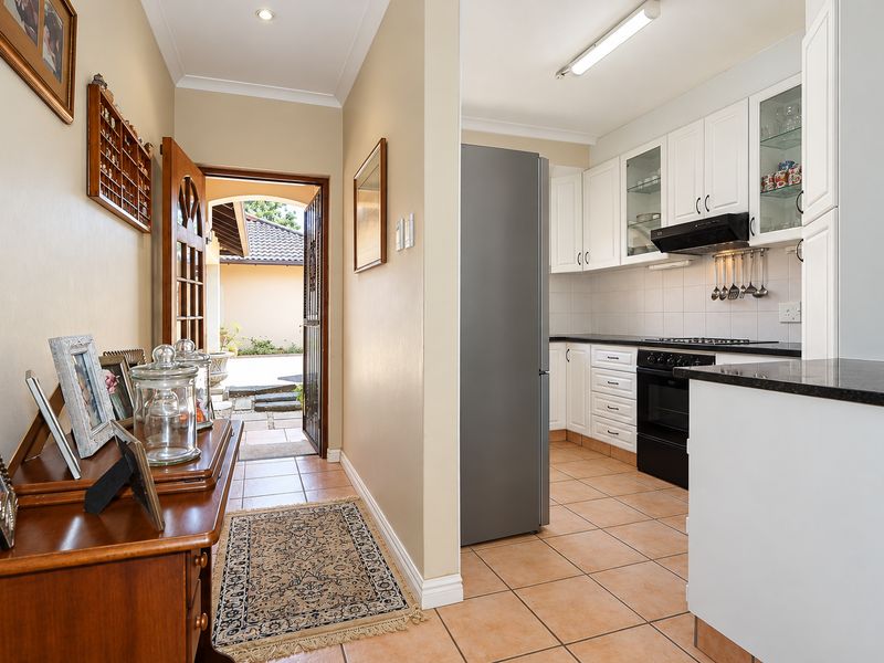 A functional kitchen featuring white cabinetry, dark stone countertops, tiled flooring, and integrated appliances, adjacent to the home entrance.
