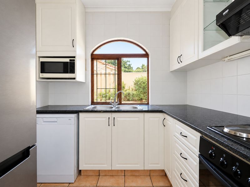 A functional kitchen featuring white cabinetry, dark granite countertops, a double basin sink, and built-in appliances including an oven, hob, and microwave.