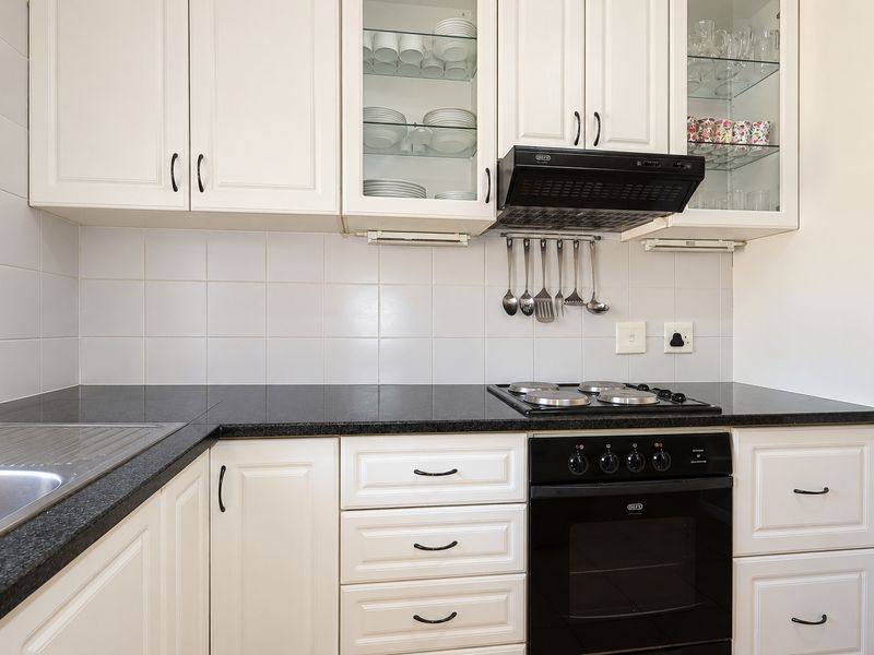 A well-maintained kitchen featuring white cabinetry, dark granite countertops, a built-in oven, hob, and extractor fan with a clean tiled backsplash.