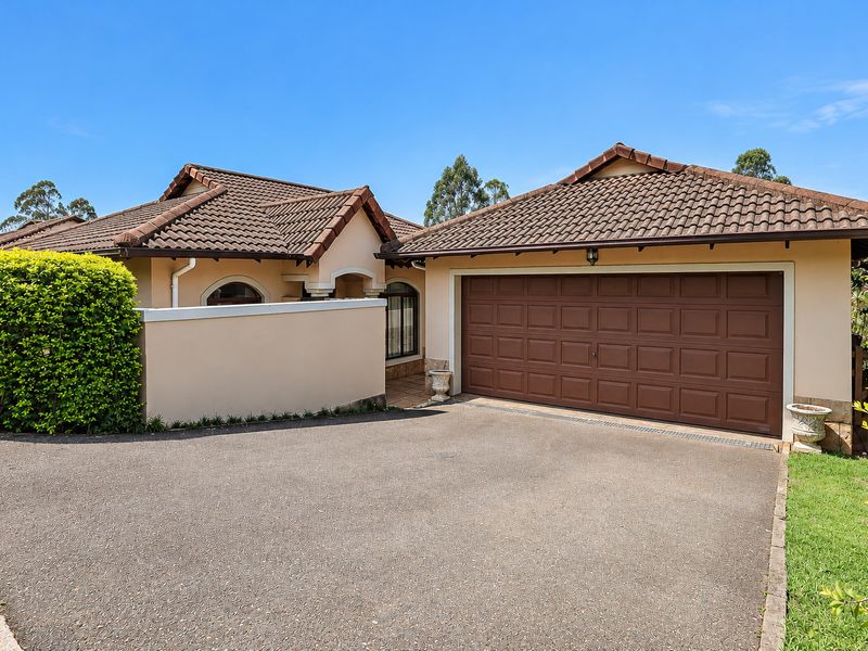 Front elevation of a townhouse featuring a paved driveway, double garage, and a private entrance archway with well-maintained exterior finishes.