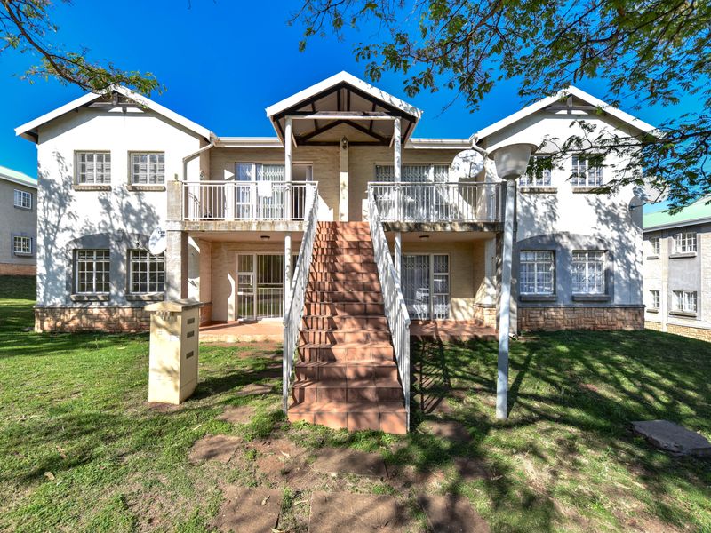 Front elevation of a two-story apartment building featuring a central tiled staircase, balconies, and stone cladding base set within a landscaped garden area.
