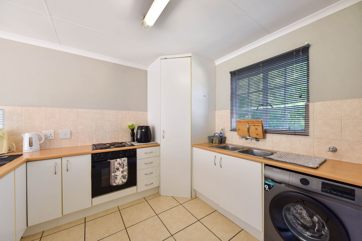 A functional kitchen featuring built-in cabinetry, laminate countertops, a double basin sink, and integrated oven and hob with tiled backsplash and flooring.