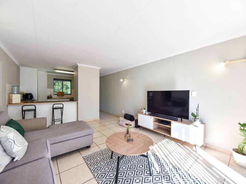 An open-plan living area featuring tiled flooring, a breakfast bar connecting to the kitchen, and neutral wall finishes.