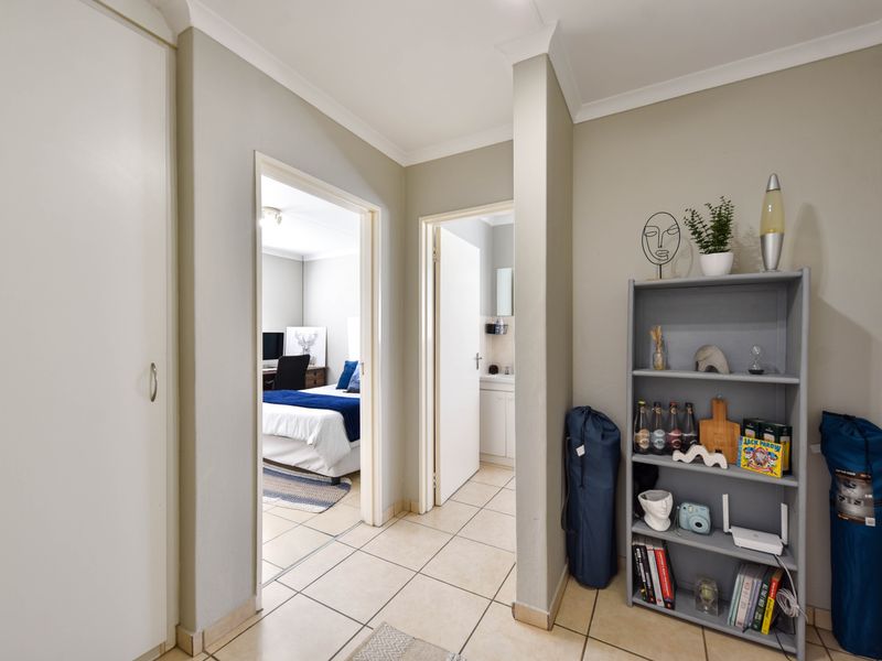 A clean and well-maintained hallway featuring tiled flooring, coved cornicing, and built-in cupboard storage, providing access to adjacent bedroom and bathroom areas.