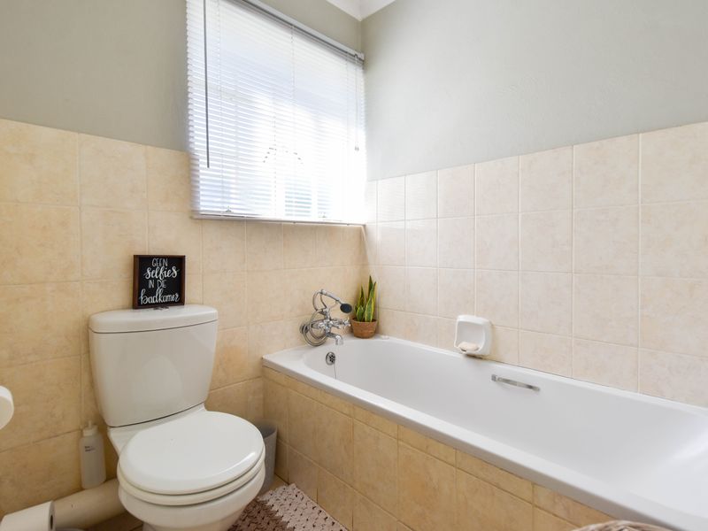 A functional bathroom featuring a standard bathtub, toilet, and neutral wall tiling with a window providing natural light.