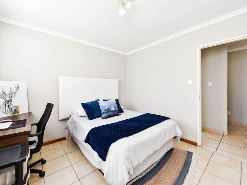 A well-maintained bedroom featuring neutral wall tones, tiled flooring, and a clean, functional layout with direct access to an adjoining hallway.
