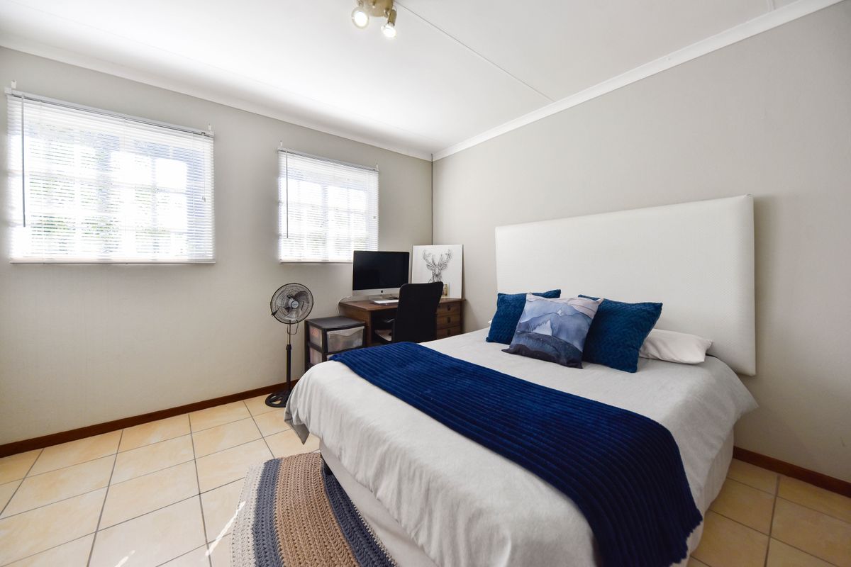 A well-maintained bedroom featuring tiled flooring, neutral wall finishes, and dual windows fitted with venetian blinds.