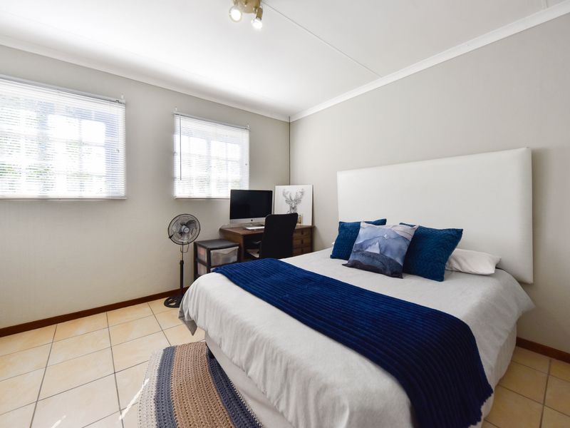 A well-maintained bedroom featuring tiled flooring, neutral wall finishes, and dual windows fitted with venetian blinds.