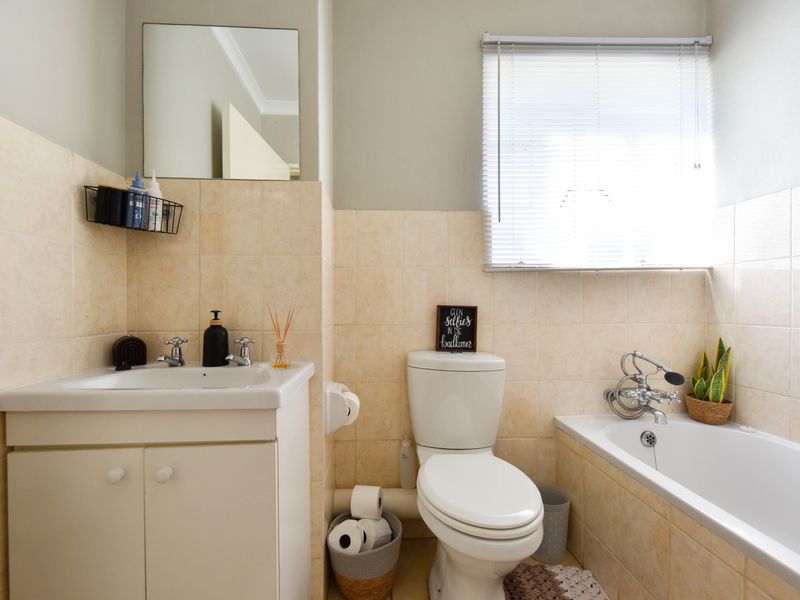 A functional bathroom featuring a vanity cabinet, toilet, and bathtub with neutral wall tiling and a window with venetian blinds.
