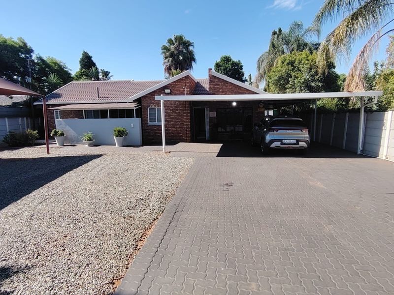 Front exterior view of a brick house featuring a paved driveway, covered carport, and low-maintenance gravel garden area.