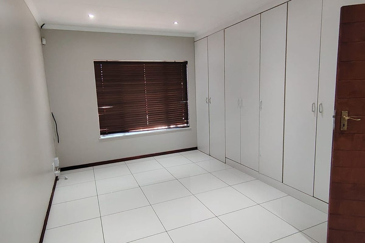 A clean, empty bedroom featuring white tiled flooring, extensive built-in cupboards, and recessed ceiling lighting.