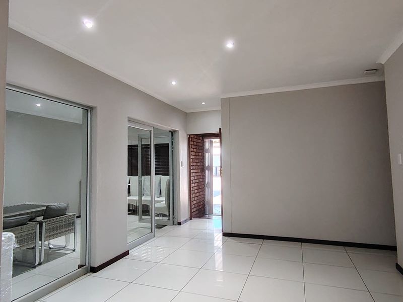 Spacious living area featuring neutral tiled flooring, recessed downlighting, and sliding glass doors leading to an adjacent room with exposed brick accents.